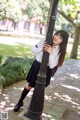 A woman in a school uniform leaning against a lamp post.