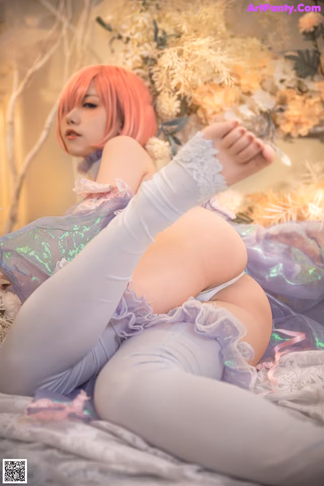 A woman with pink hair is sitting on a bed.