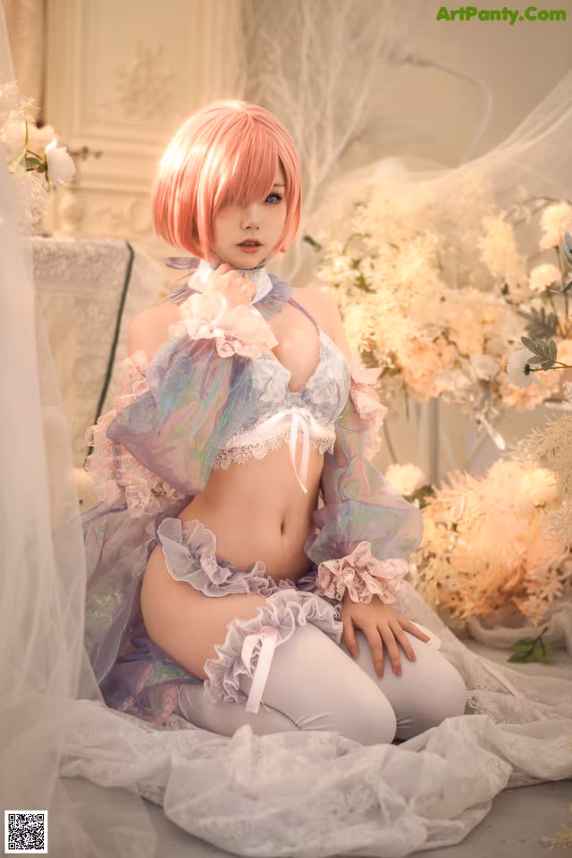 A woman with pink hair sitting on a bed.