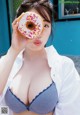 A woman holding a donut in front of her face.