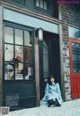 A woman sitting on the sidewalk in front of a store.