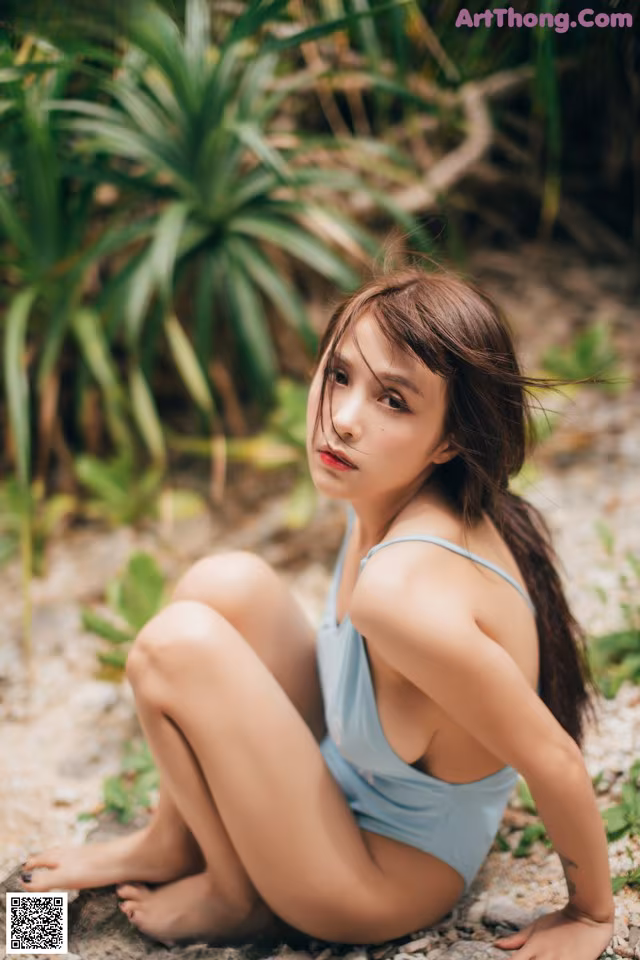 A woman in a blue bathing suit sitting on a rock.