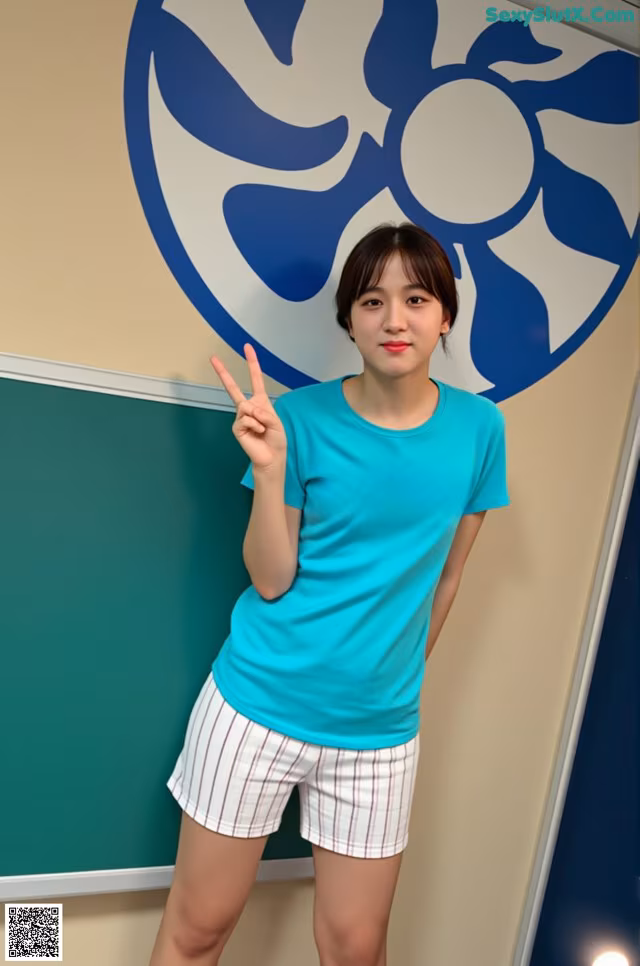 A woman standing in front of a green wall holding up a peace sign.