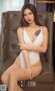 A woman in a white bodysuit sitting on a brown chair.