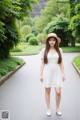 A woman in a white dress and hat standing on a road.