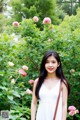 A woman standing in front of a bush of pink roses.