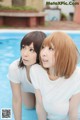 A couple of young women standing next to a swimming pool.