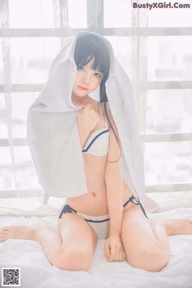 A woman in a white bikini sitting on a bed.