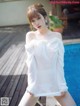 A woman in a white dress posing by a pool.