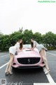 A couple of women standing next to a pink car.