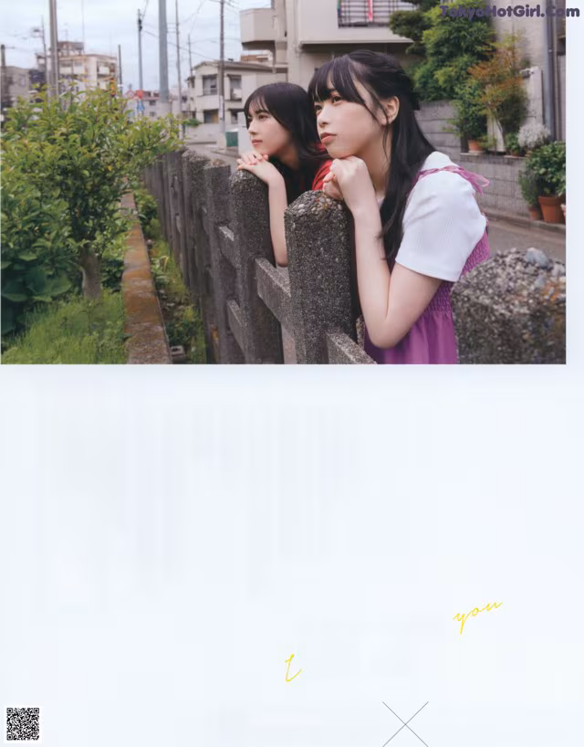 A couple of young women standing next to each other near a fence.