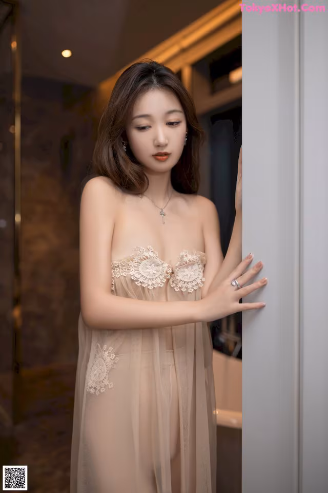 A woman in a nude lingerie leaning against a wall.