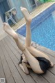 A woman laying on a wooden deck next to a swimming pool.