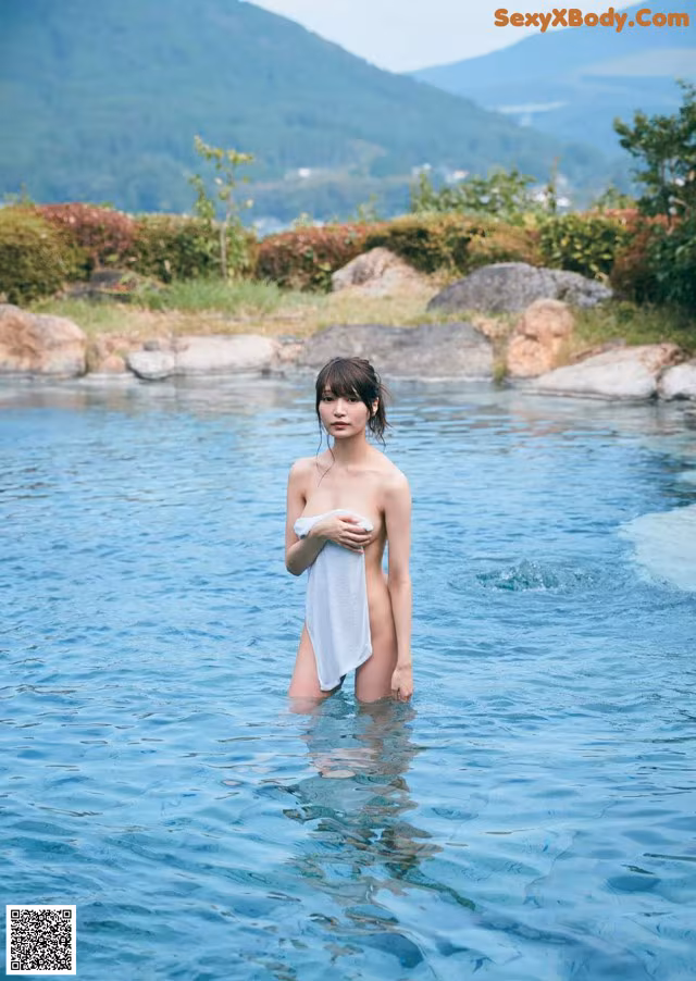 A woman standing in a body of water holding a towel.