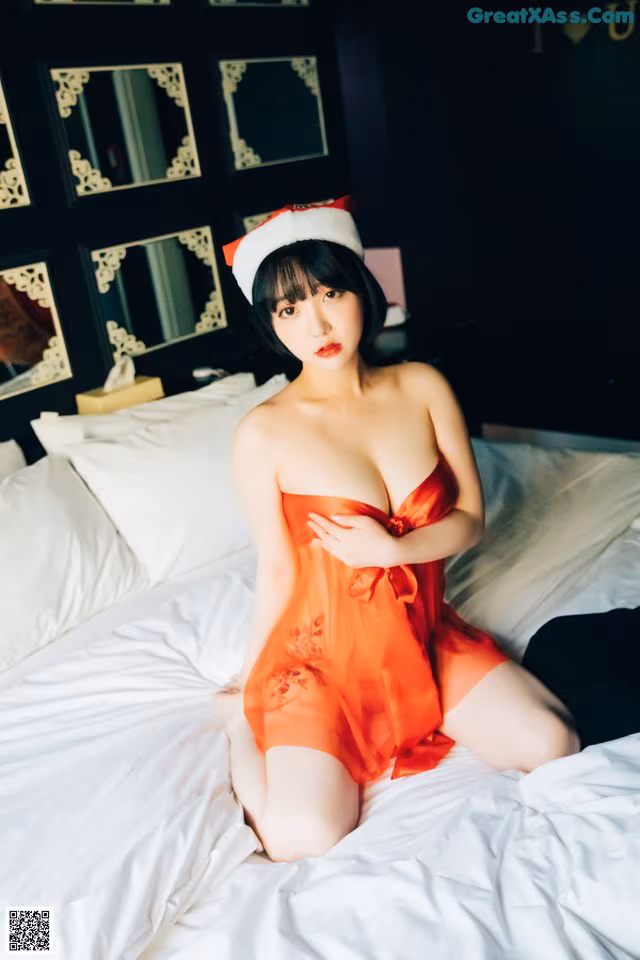 A woman in a red dress sitting on a bed.