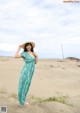 A woman in a green dress and straw hat standing on a beach.