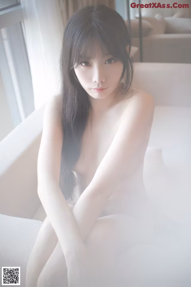 A naked woman sitting on a white couch.