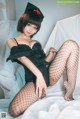 A woman in a black dress and fishnet stockings sitting on a bed.