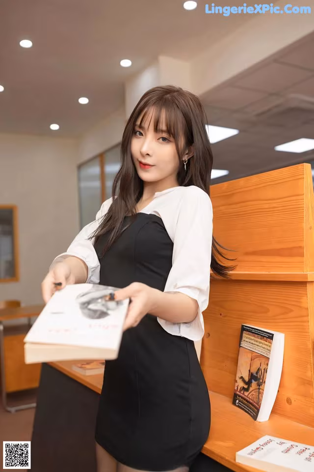 A woman in a black dress holding a book.